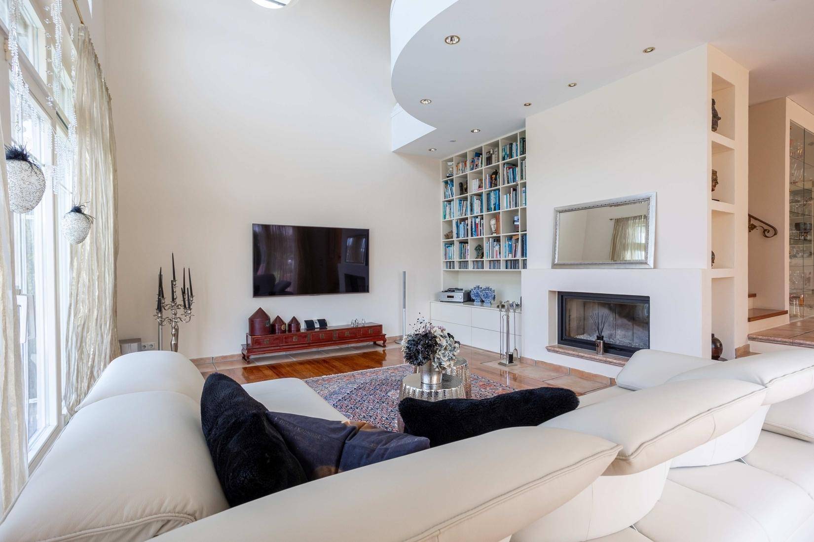 Modern eingerichtetes Wohnzimmer mit großem Fernseher, Kamin und hohen Decken.