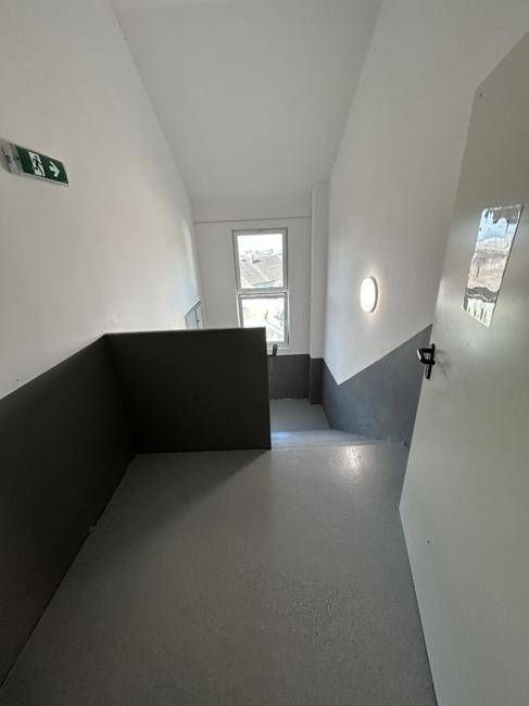 Helles Treppenhaus mit grauen Stufen und einem Fenster, das natürliches Licht hereinlässt.
