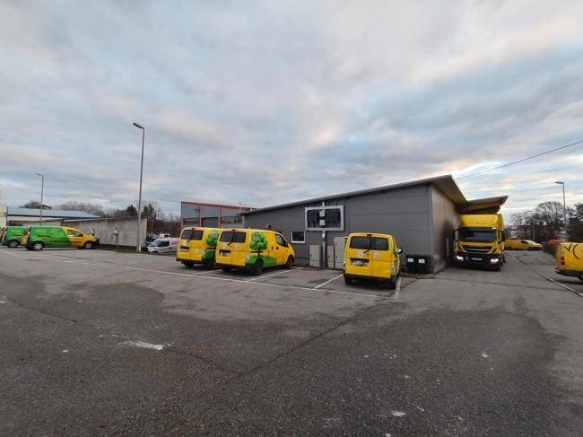 Gesamtansicht des Geschäftsgebäudes mit großem Parkplatz und vielen geparkten Lieferwagen.