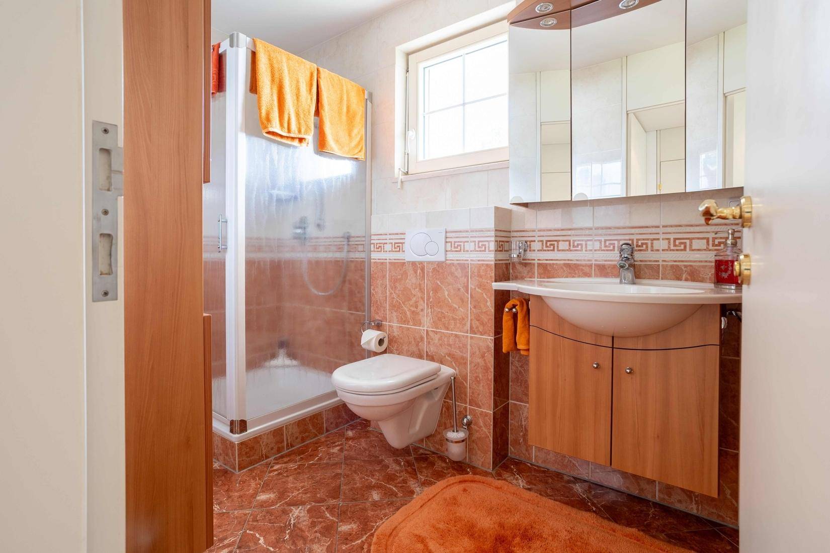 Funktionales Badezimmer mit Dusche, WC und Fenster, in warmen Erdtönen gefliest.