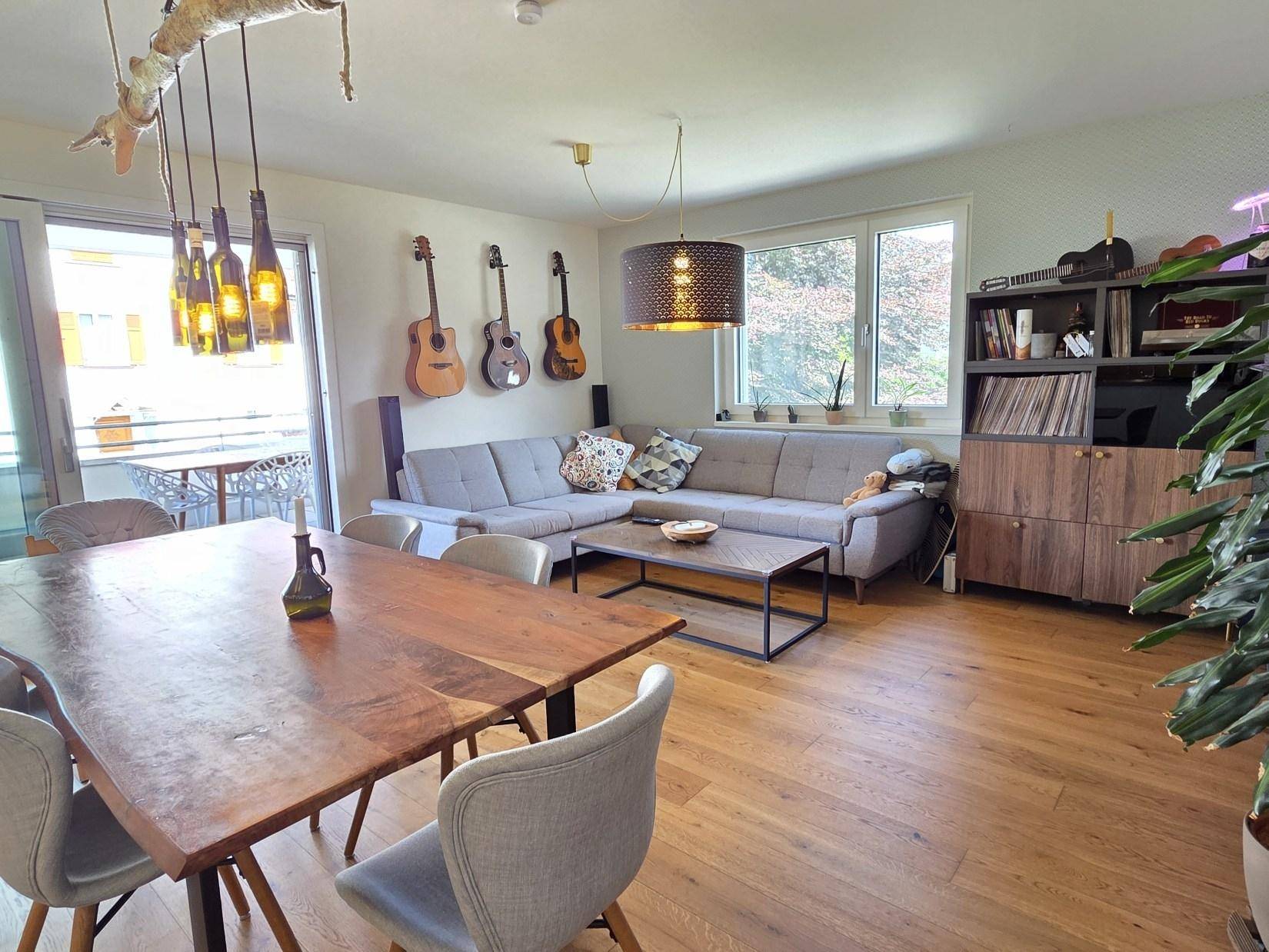 Helles Wohn- und Esszimmer mit Holzboden, bequemer Couch und Zugang zum Balkon.