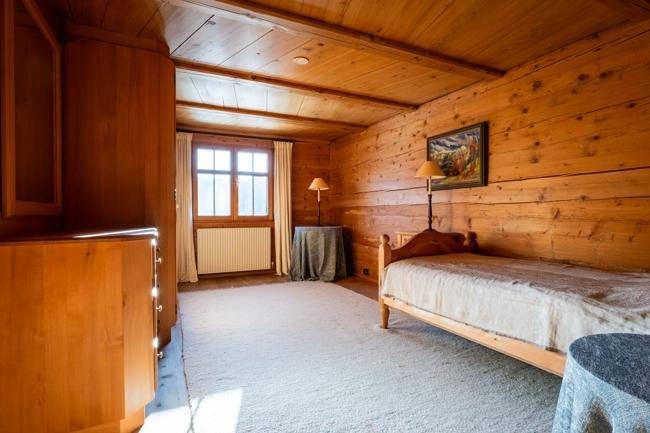 Einzelzimmer mit Holzwänden und -decke, einem Einzelbett und einem Fenster, das den Raum erhellt.