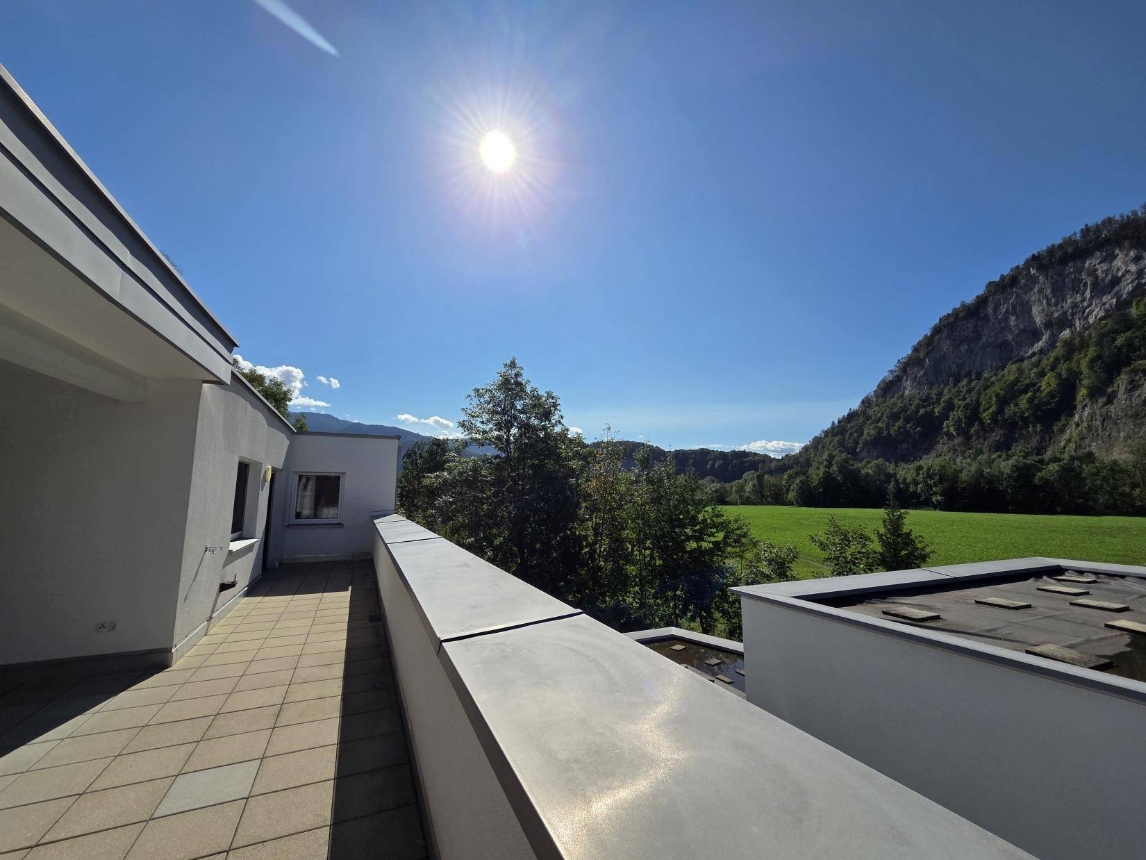 Sonniger Ausblick von der Terrasse auf grüne Wiesen und die majestätische Bergkulisse.