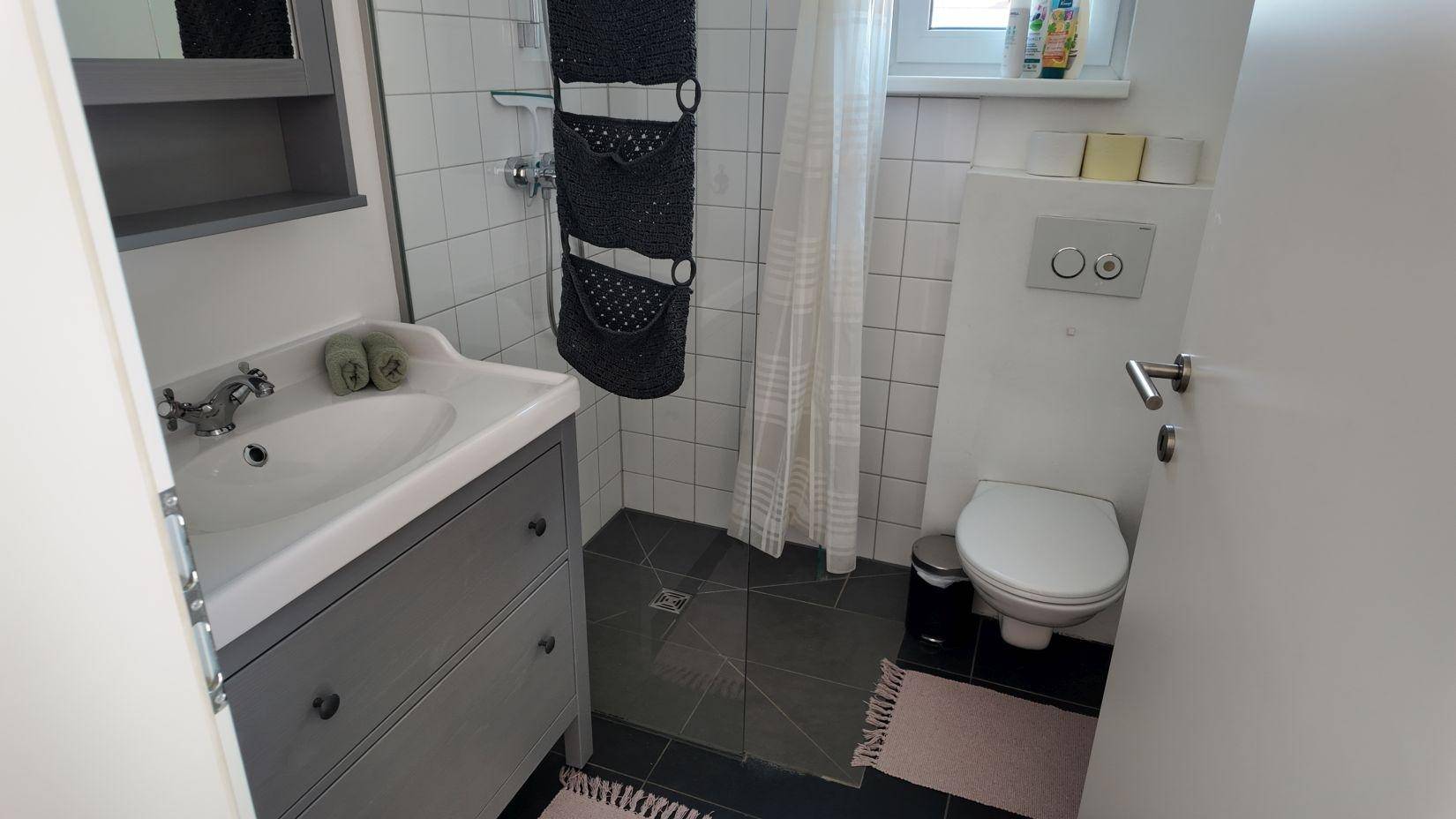 Kleines, hell gefliestes Badezimmer mit Dusche, Waschbecken und wandhängendem WC in modernem Design.