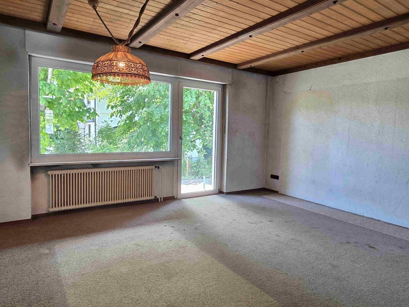 Helles Wohnzimmer mit Teppichboden, Holzdecke und Zugang zu einem Außenbereich.