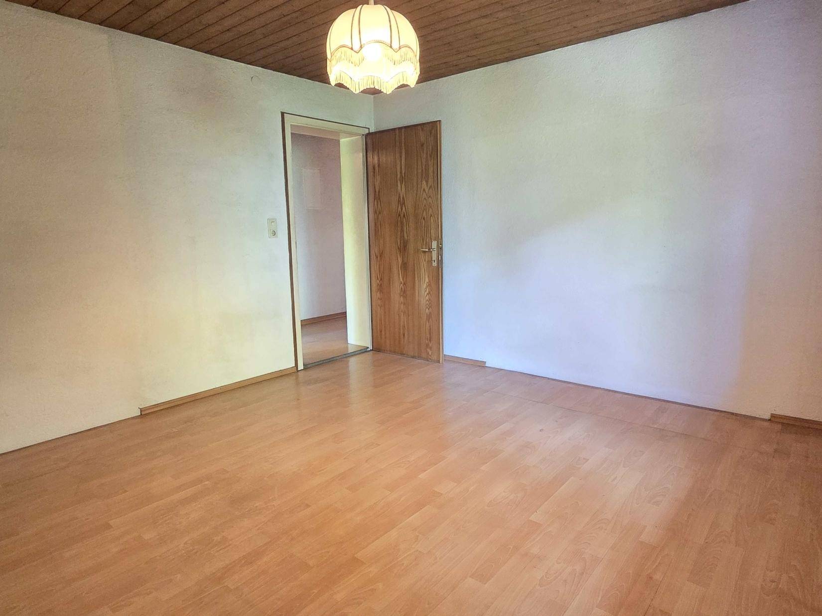 Helles Schlafzimmer mit Laminatboden, Holztür und Holzdecke, bereit zur Gestaltung.