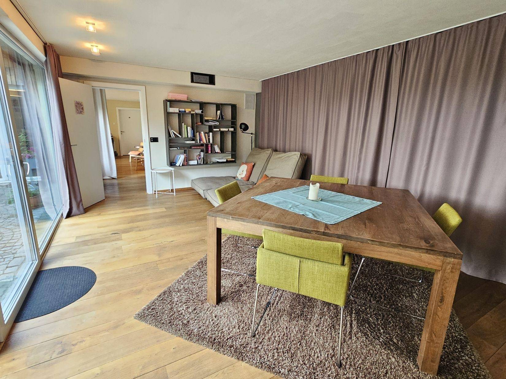 Gemütlicher Essbereich mit Holztisch und grünen Stühlen, angrenzend an einen Wohnbereich mit Sofa.