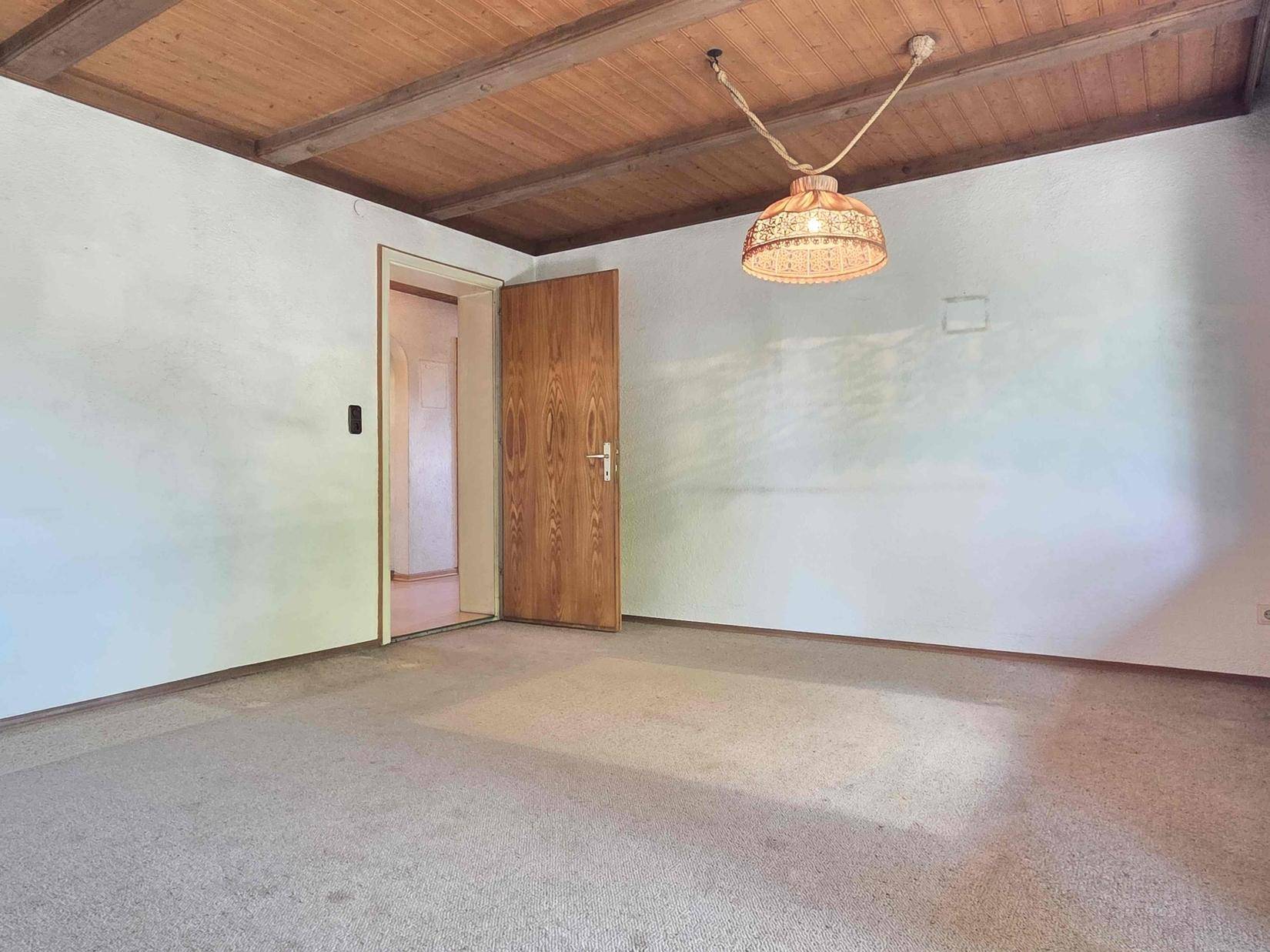 Wohnzimmer mit Teppichboden, Holztür und Holzdecke, bereit zur individuellen Gestaltung.