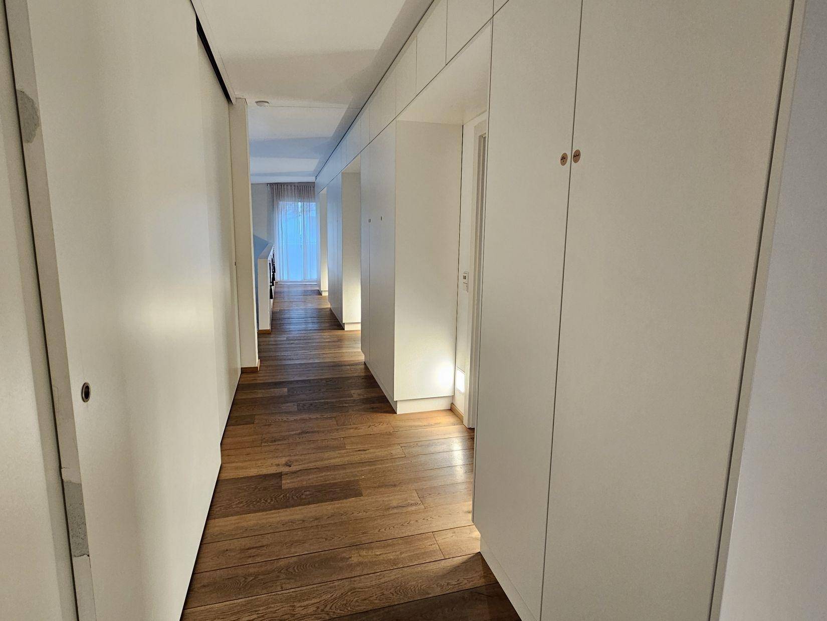 Langer Flur mit integrierten weißen Einbauschränken und Holzboden, der viel Stauraum bietet.