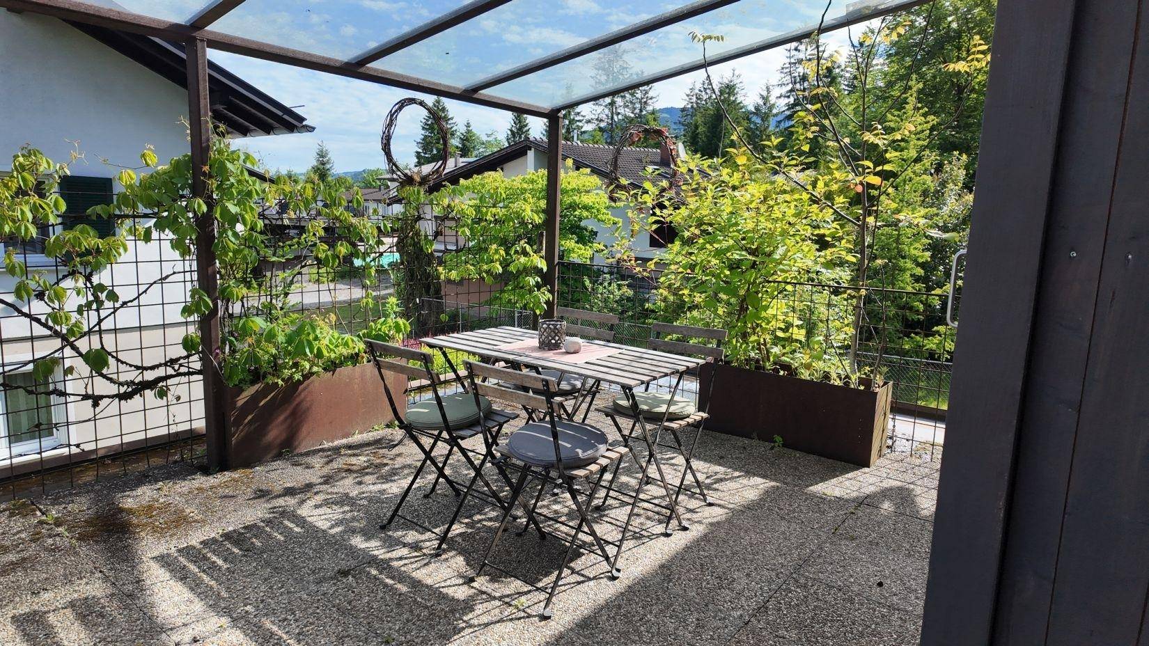 Überdachte Terrasse mit Gartenmöbeln und üppiger Bepflanzung, ideal zum Entspannen im Freien.