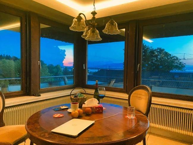 Gemütlicher Essbereich mit Holztisch und weitem Blick auf den See und die Landschaft bei Sonnenuntergang.