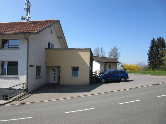 Vorderansicht des Gebäudes mit Eingangsbereich und Parkplatz unter klarem blauem Himmel.