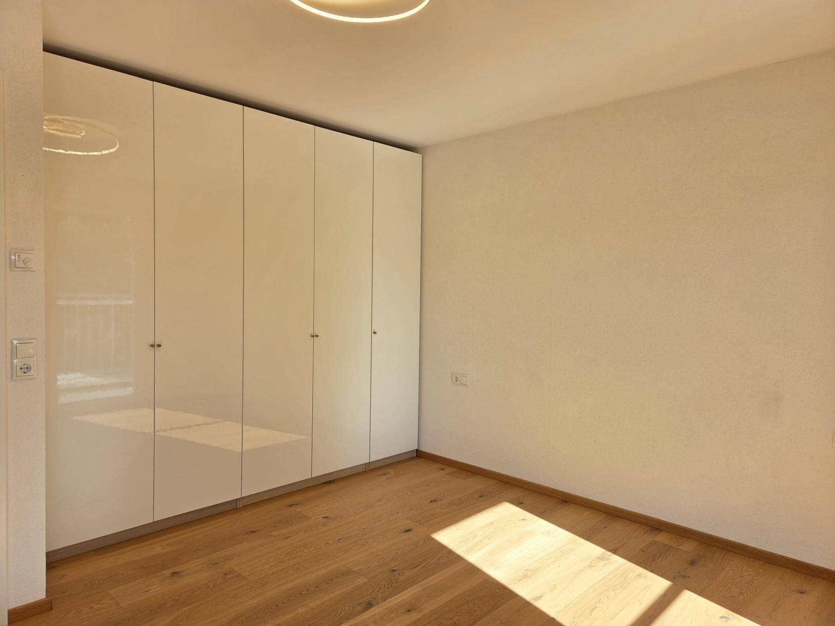 Schlafzimmer mit Eichenparkett und großem, glänzendem Einbauschrank entlang einer Wand.
