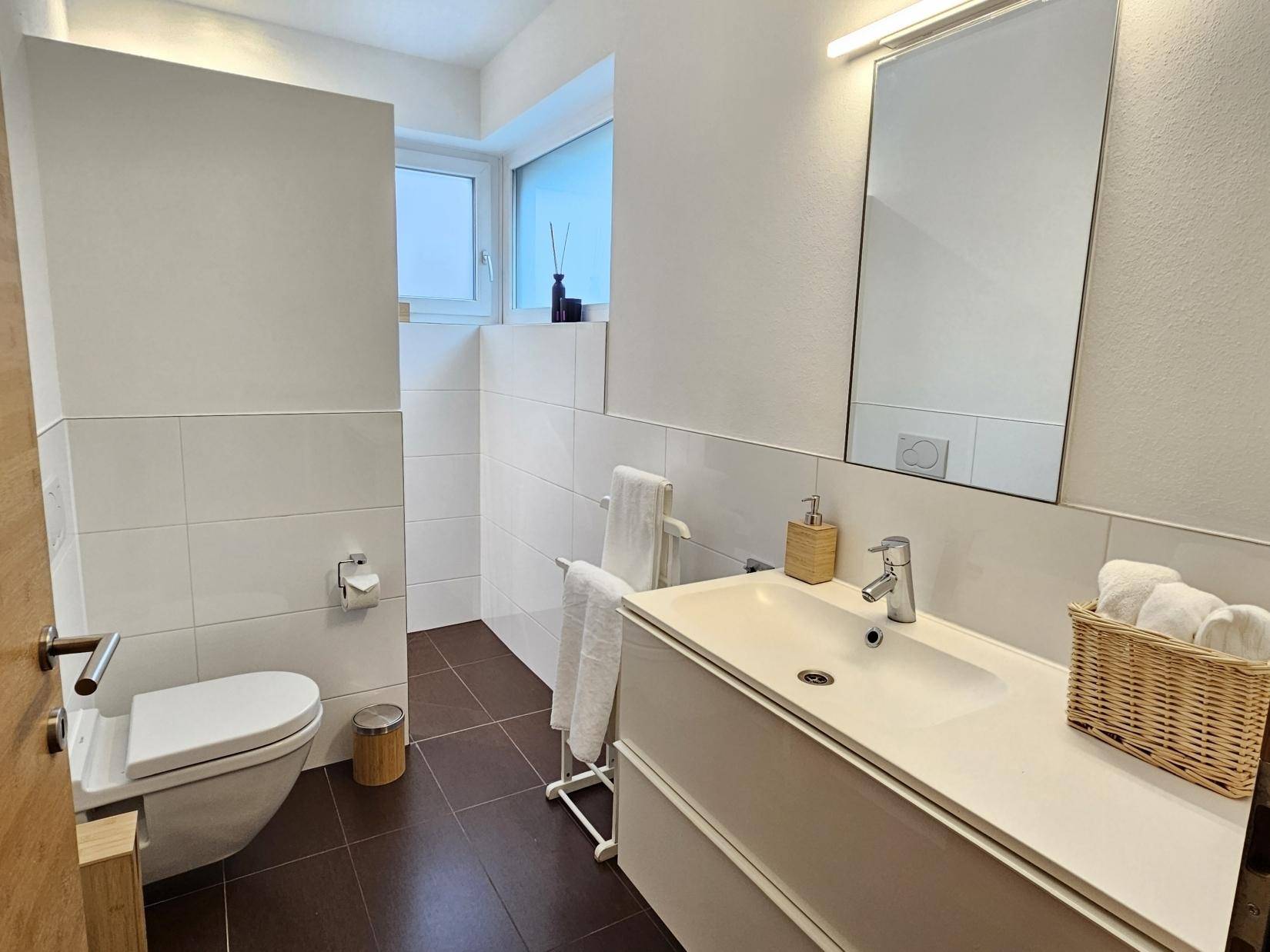 Modernes Badezimmer mit weißem Waschtisch, Wand-WC und braunen Bodenfliesen.