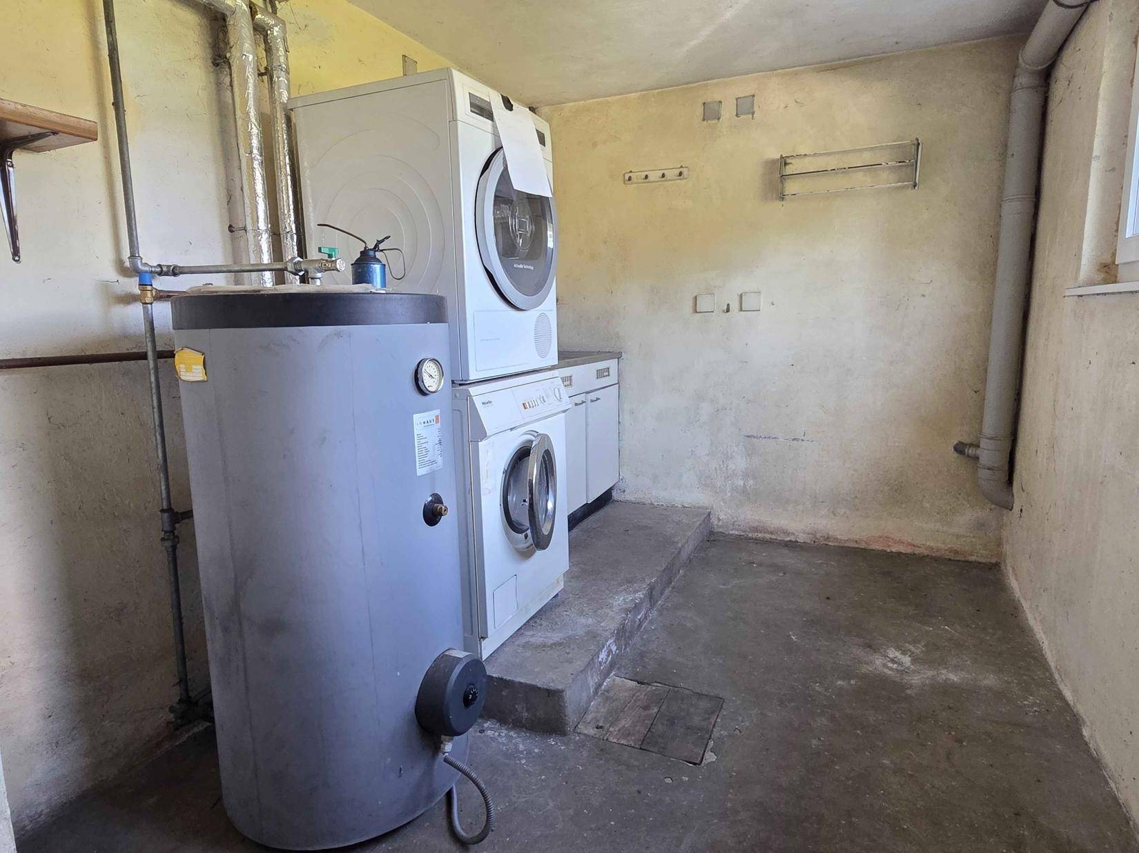 Waschküche im Keller mit Waschmaschine, Trockner und Warmwasserspeicher.
