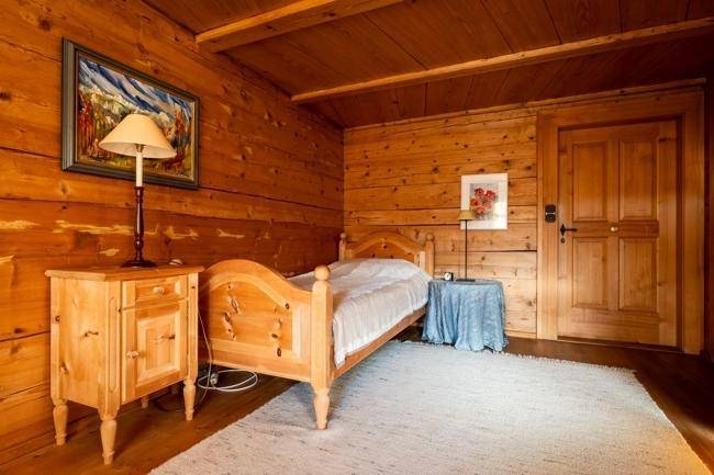 Kleines Schlafzimmer mit Holzwänden, Einzelbett und einem Nachttisch mit Lampe, der eine warme Atmosphäre schafft.