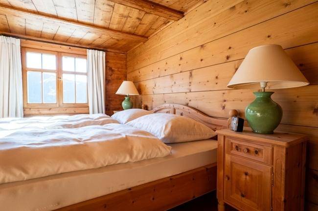 Gemütliches Schlafzimmer mit Holzwänden und -decke, einem Doppelbett und Blick auf die Berge durch das Fenster.