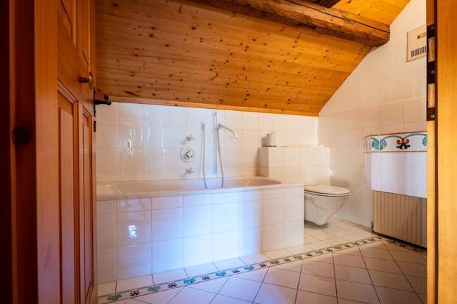 Dachgeschoss-Badezimmer mit Badewanne, WC und weißen Fliesen, die einen traditionellen Charme verleihen.