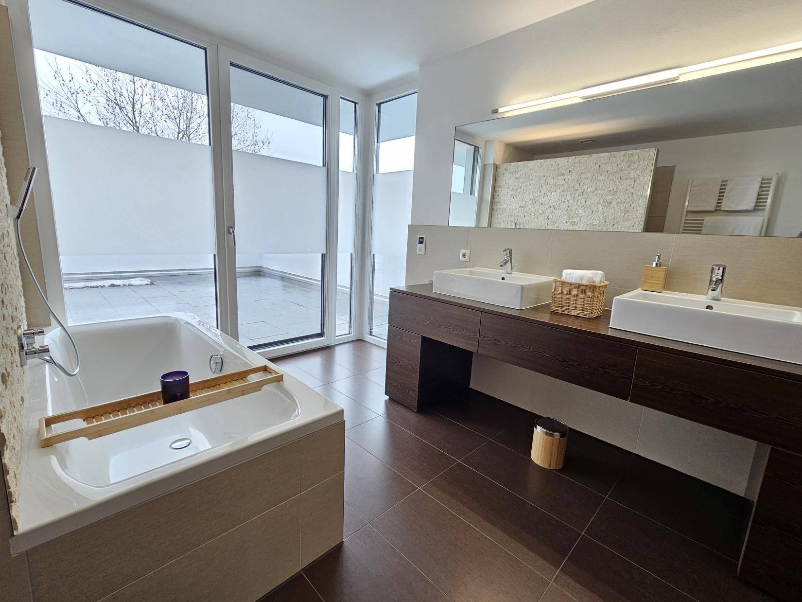 Modernes Badezimmer mit Doppelwaschbecken, Badewanne und Zugang zu einer privaten Terrasse.