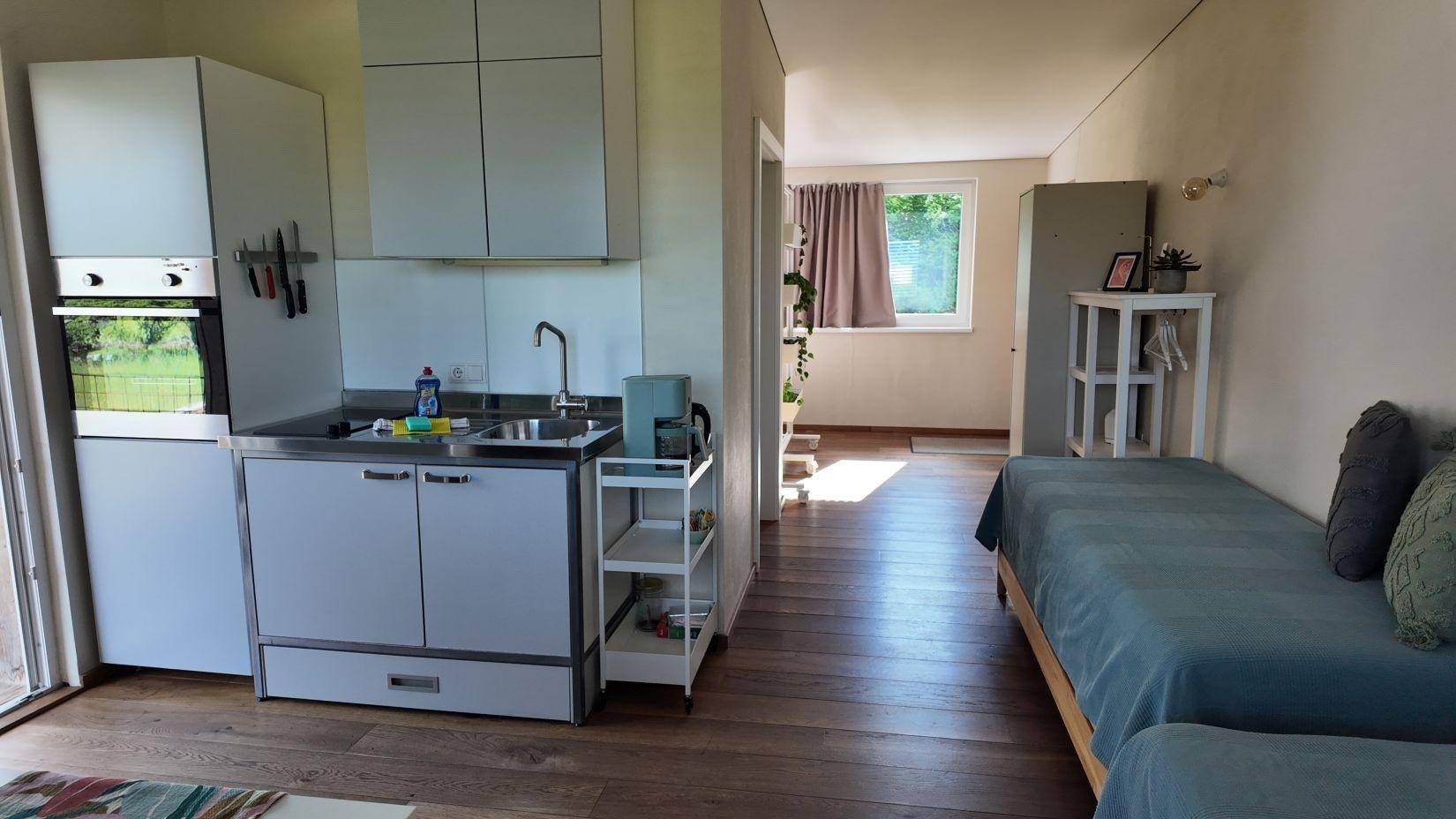 Kombinierter Schlafbereich mit zwei Einzelbetten, kleiner Küchenzeile und Holzboden.