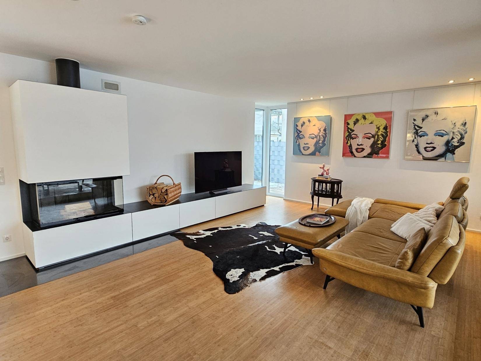 Helles Wohnzimmer mit modernem Kamin, Holzboden und Pop-Art-Dekoration.