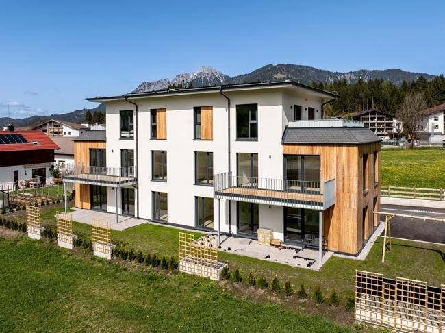 Moderne Wohnanlage mit weißer Fassade, Holzverkleidung und Balkonen in alpiner Umgebung.