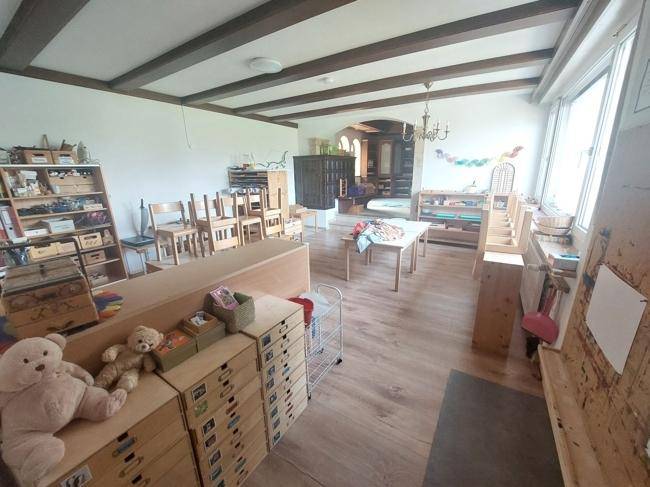 Heller Innenraum mit Holzbalkendecke, Kindermöbeln und Spielzeug, ideal als Spielzimmer.