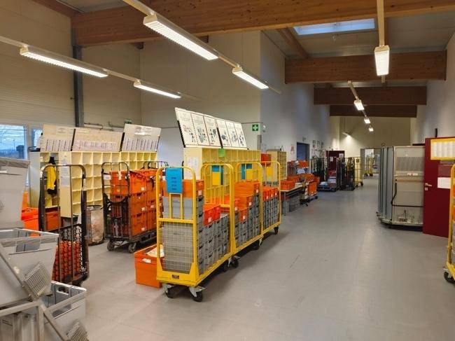 Langer Gang im Sortierbereich mit zahlreichen gelben Rollwagen und Postsendungen.