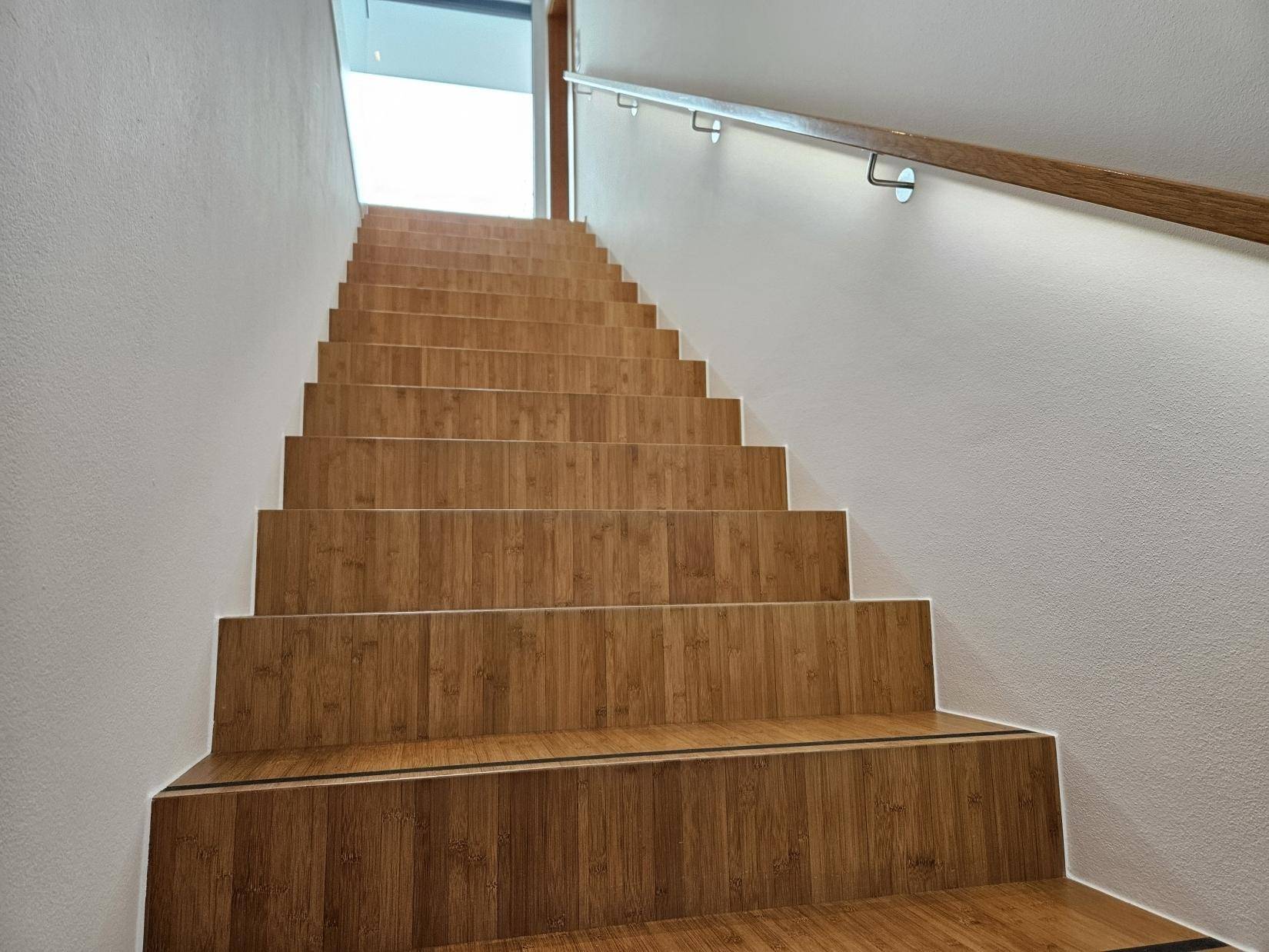 Holztreppe mit Handlauf und hellem Aufgang zu den oberen Etagen.