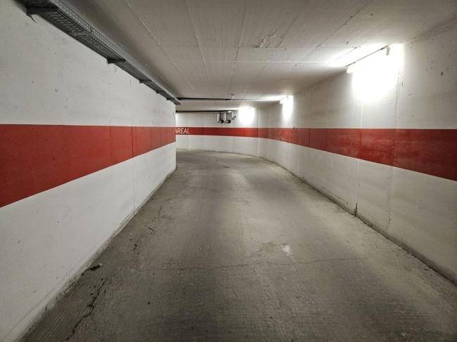 Lange, kurvige Zufahrt zu einer Tiefgarage mit weiß-roten Wänden und Beleuchtung.