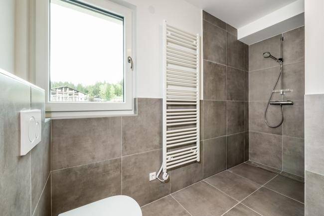 Modernes Badezimmer mit ebenerdiger Dusche, grauen Fliesen und beheiztem Handtuchhalter.