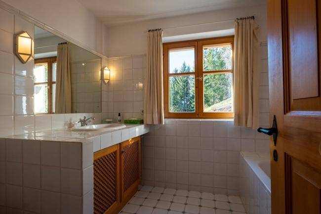 Helles Badezimmer mit weißen Fliesen, einem Waschbecken und einem Fenster mit Blick auf die Natur.