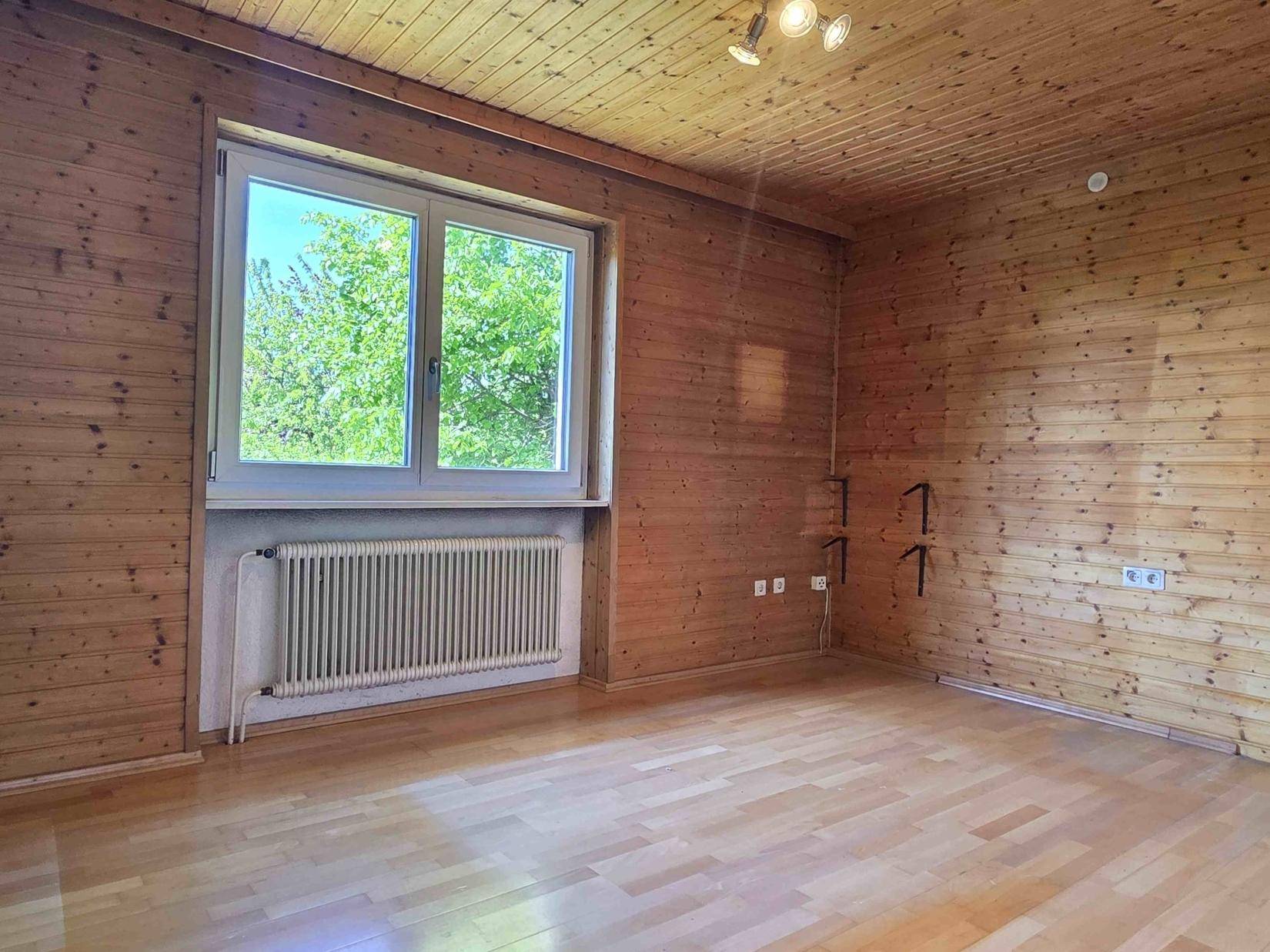 Geräumiges Schlafzimmer mit Holzwänden, Holzdecke und Laminatboden, hell durch großes Fenster.