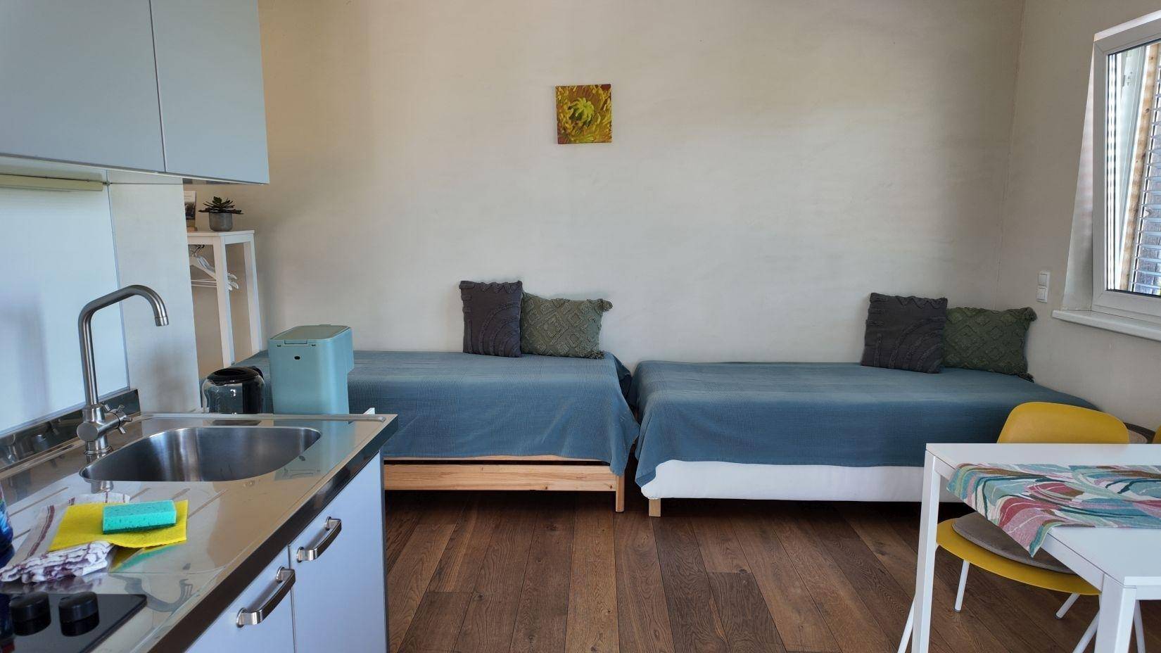 Helles Schlafzimmer mit zwei Einzelbetten, Holzboden und einer kleinen Essecke mit farbenfroher Dekoration.