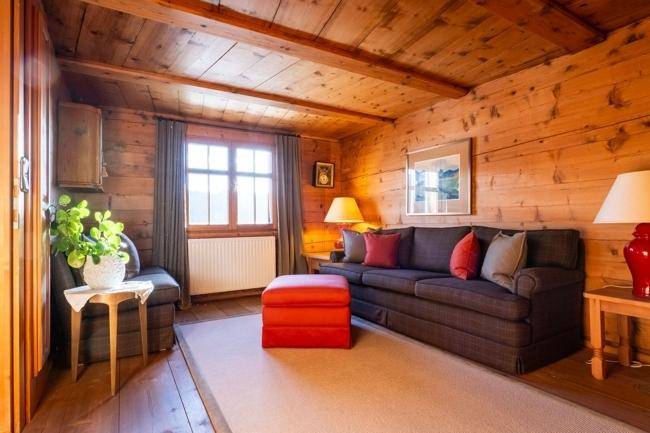 Rustikales Wohnzimmer mit Holzwänden, Holzbalkendecke und bequemen Sofas.