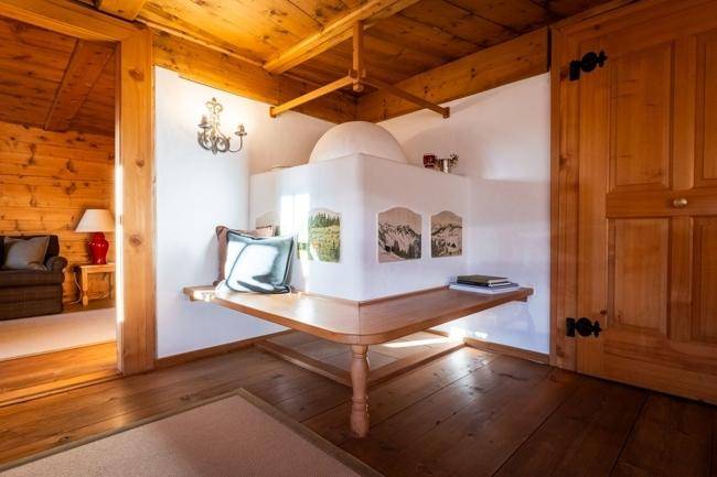 Gemütliche Sitzecke mit traditionellem Kachelofen und Holzboden in einem hellen Raum.