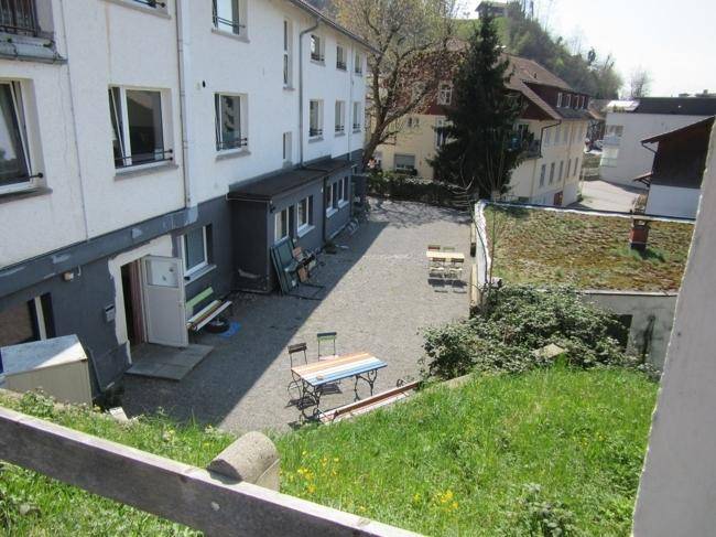 Hinterhofbereich des Gebäudes mit Kiesfläche, Sitzgelegenheiten und angrenzender Grünfläche.