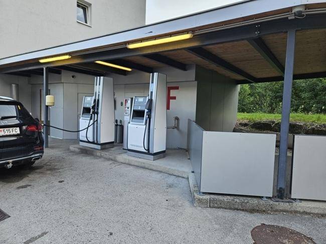 Detailansicht einer Tankstelle mit zwei Zapfsäulen und einem geparkten Auto unter einem Vordach.