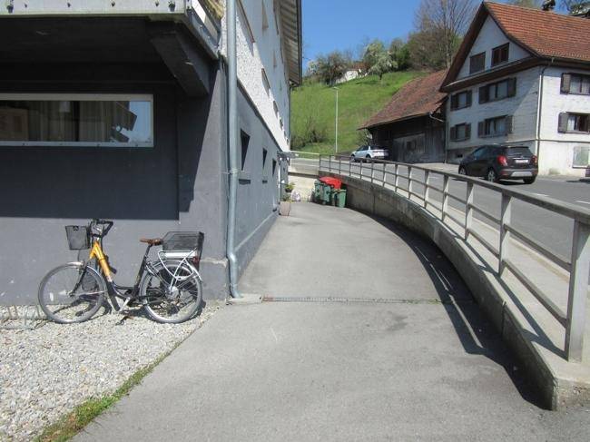 Barrierefreie Rampe entlang der Gebäudeseite mit Blick auf die Straße und angrenzende Natur.