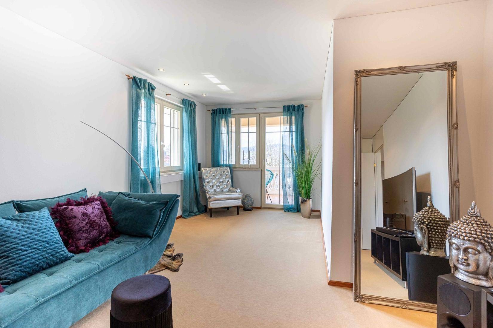 Heller Wohnbereich mit großem Spiegel, Sofa und Zugang zu einem Balkon.
