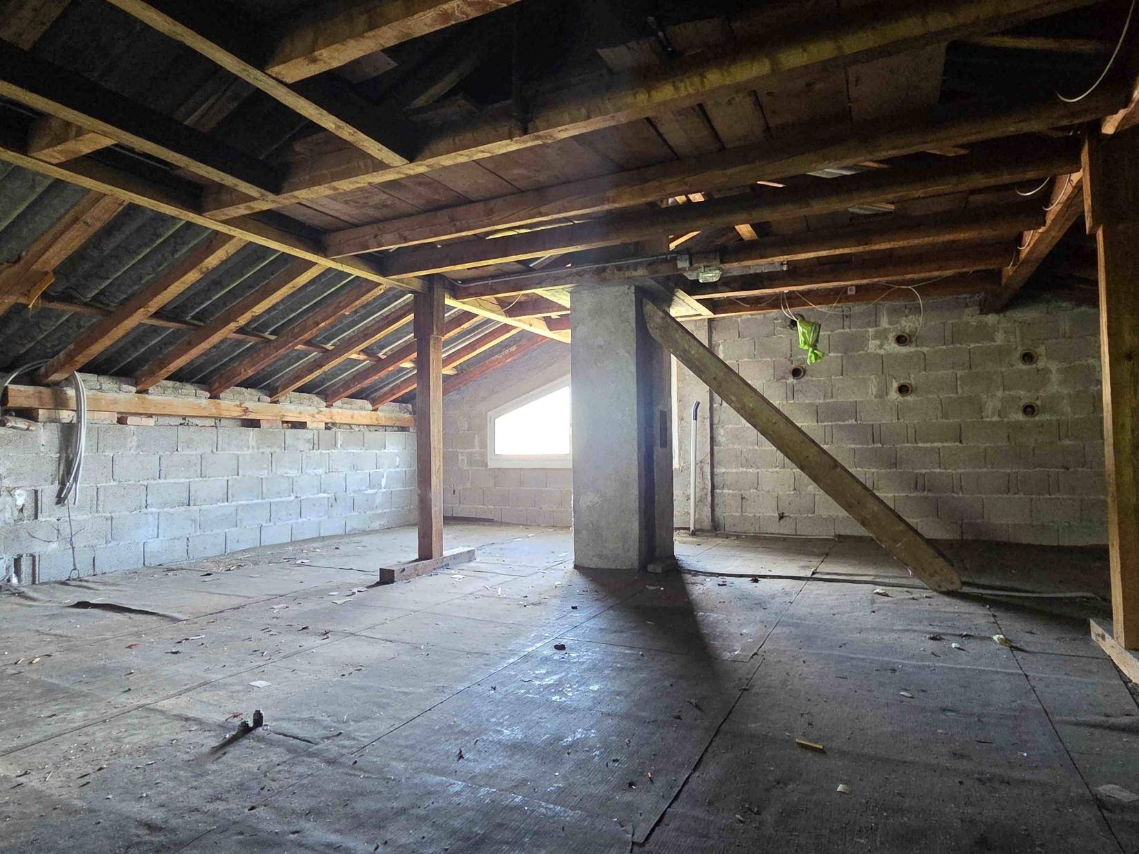 Großer Dachboden mit Holzbalken und Fenster, ideal für zukünftige Wohnraumerweiterung.