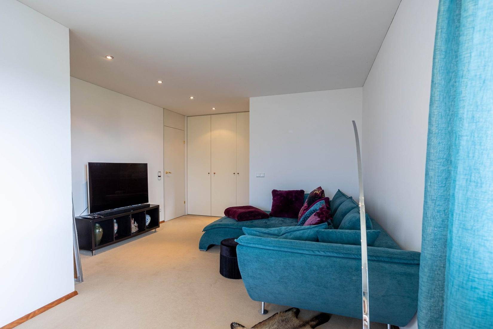 Gemütlicher Wohnbereich mit Sofa, Fernseher und Zugang zu einem Balkon.