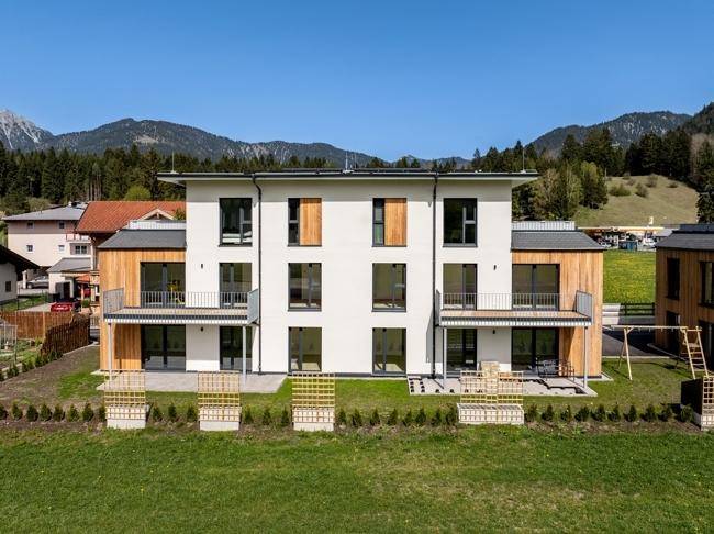 Vorderansicht der modernen Wohnanlage mit weißer Fassade, Holzdetails und Balkonen.