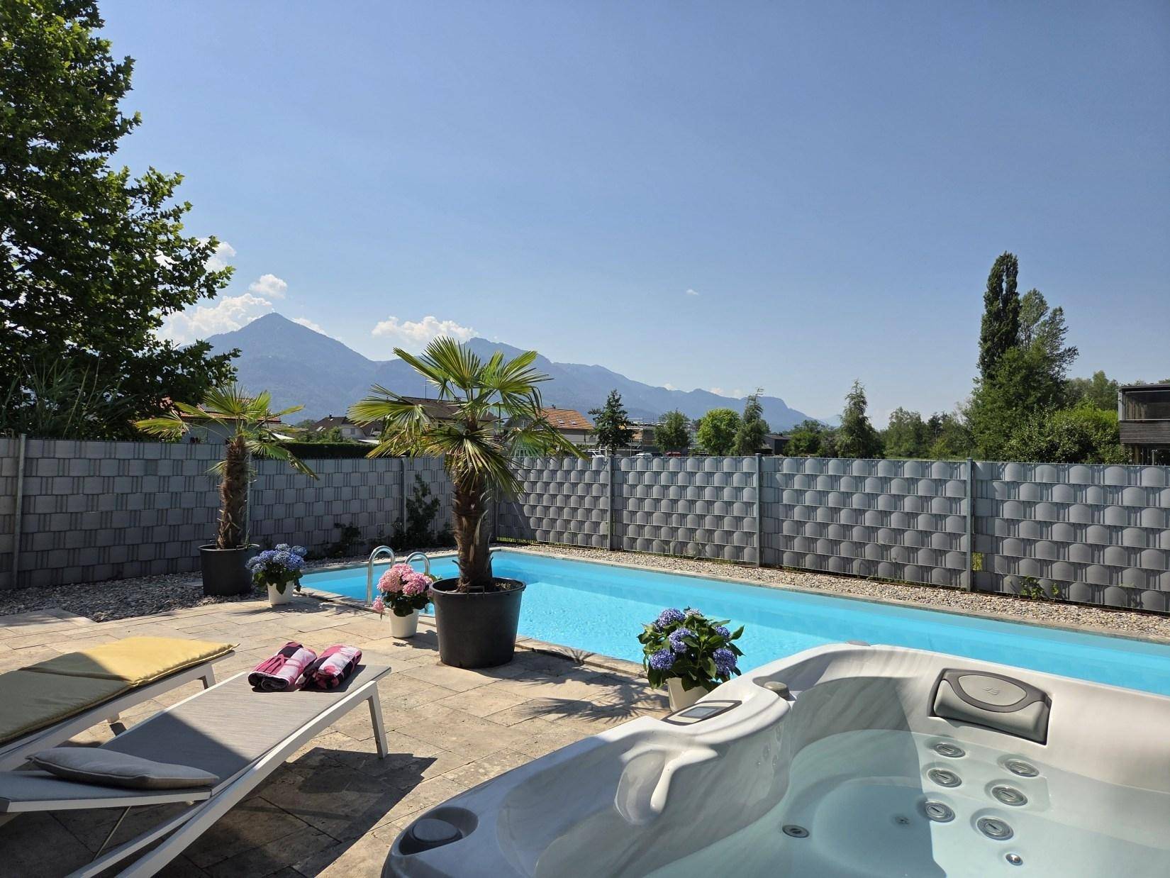 Entspannungsbereich mit Whirlpool und Pool, umgeben von Liegestühlen und mit malerischem Bergblick.