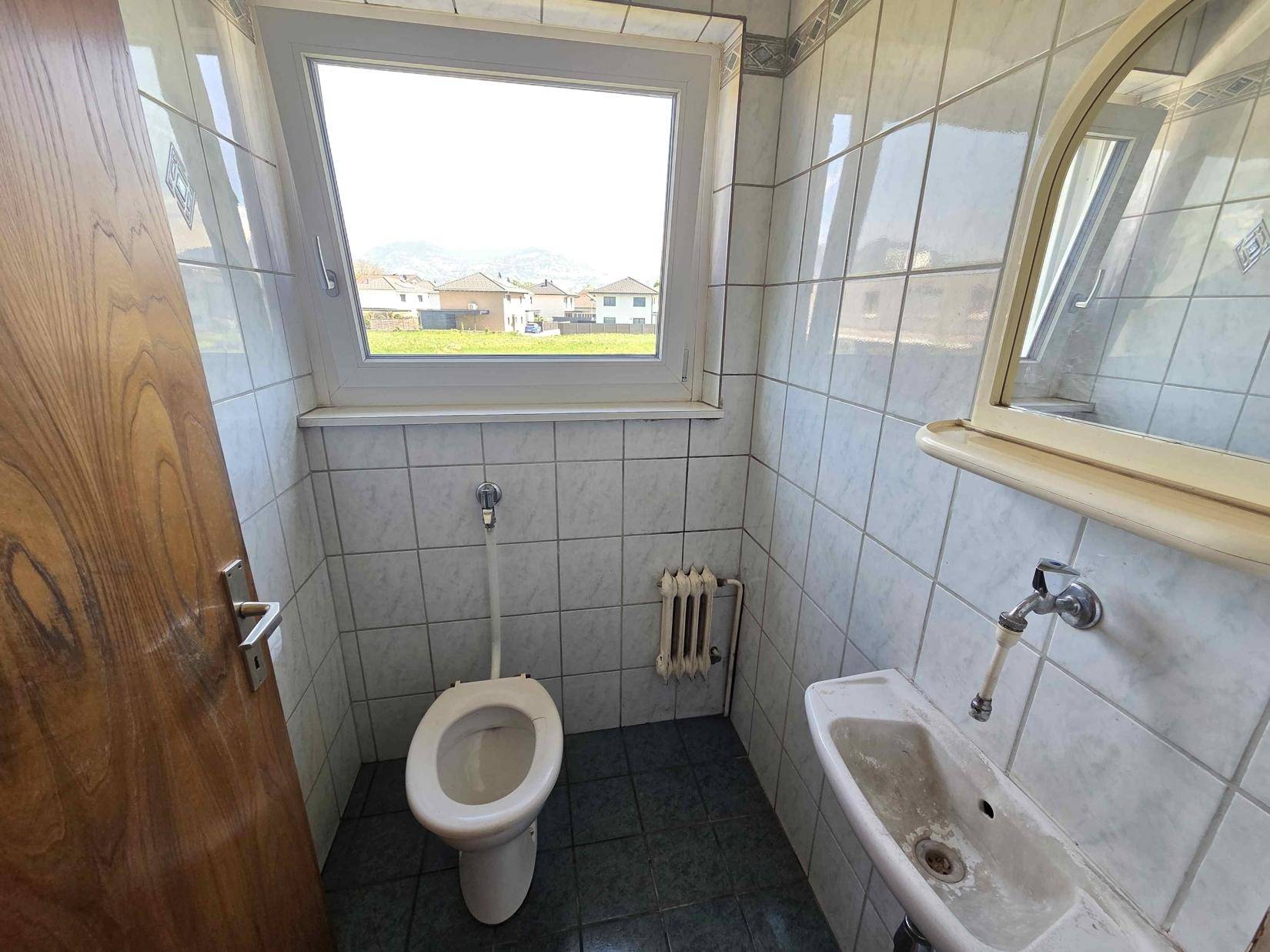Separate Toilette mit WC, kleinem Waschbecken und Fenster, im älteren Stil gefliest.