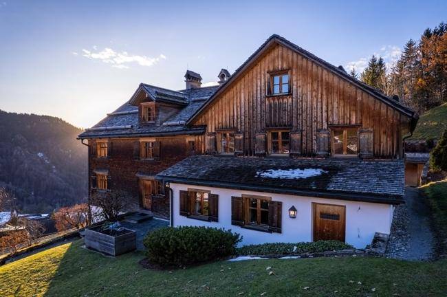 Detailansicht der Holzfassade des Hauses mit traditionellen Fensterläden und einem Anbau im Sonnenlicht.