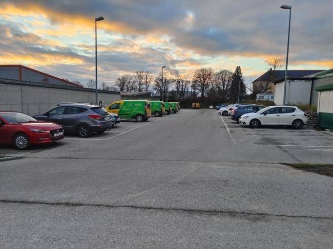 Großer Parkplatz mit verschiedenen Fahrzeugen unter einem bewölkten Himmel.