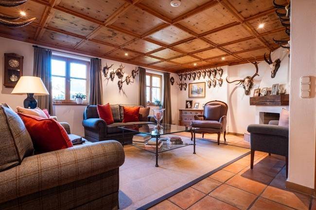 Großzügiges Wohnzimmer im alpinen Stil mit Kamin, Kassettendecke und Jagdtrophäen.