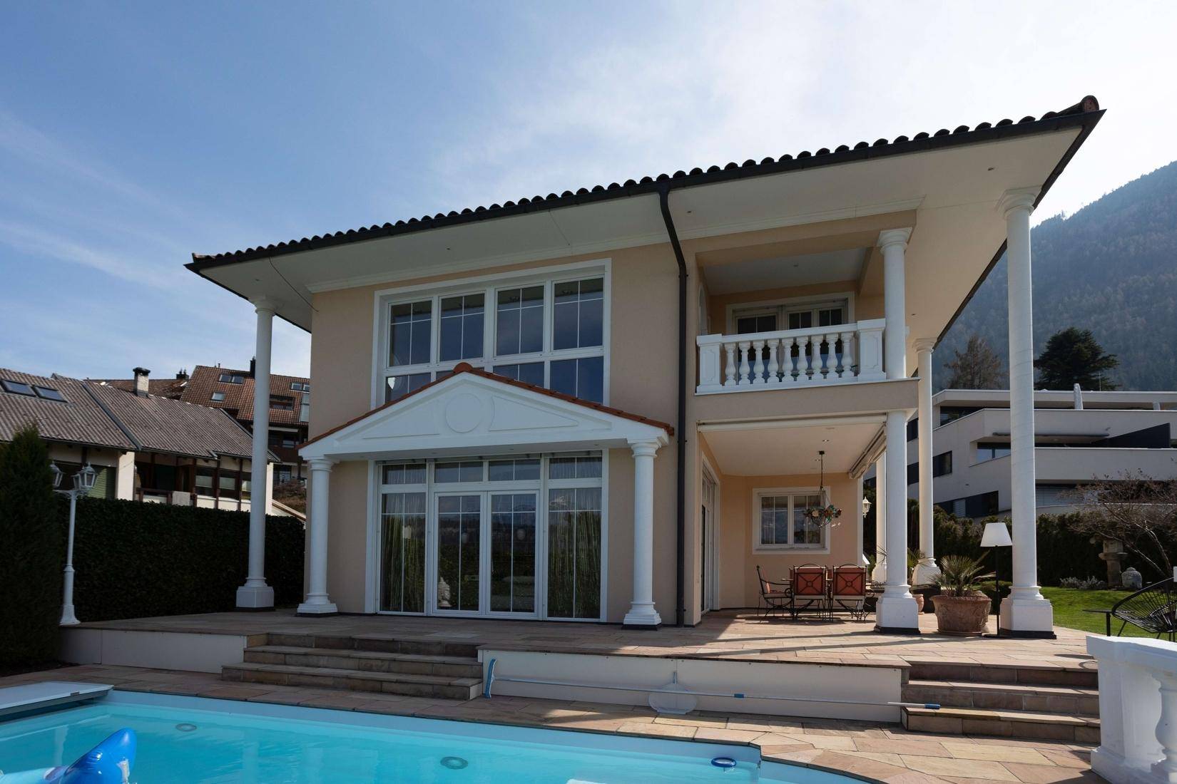 Elegante Villa mit großem Poolbereich und sonniger Terrasse, umgeben von grüner Landschaft.