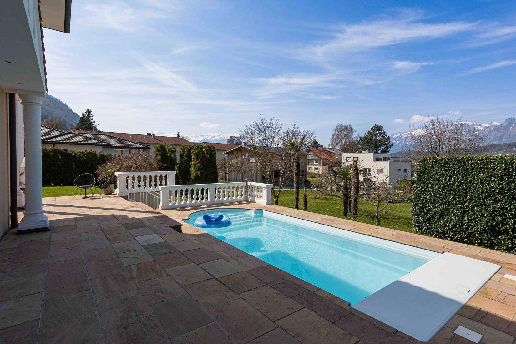 Langer, rechteckiger Pool mit Steinfliesen und Blick auf die grüne Umgebung.
